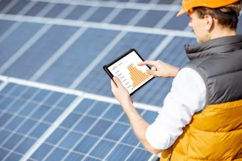 Eine Solarinstallateur analysiert mit seinem Tablet und einer speziellen Software die Effektivität der Solaranlage im Hintegrund.